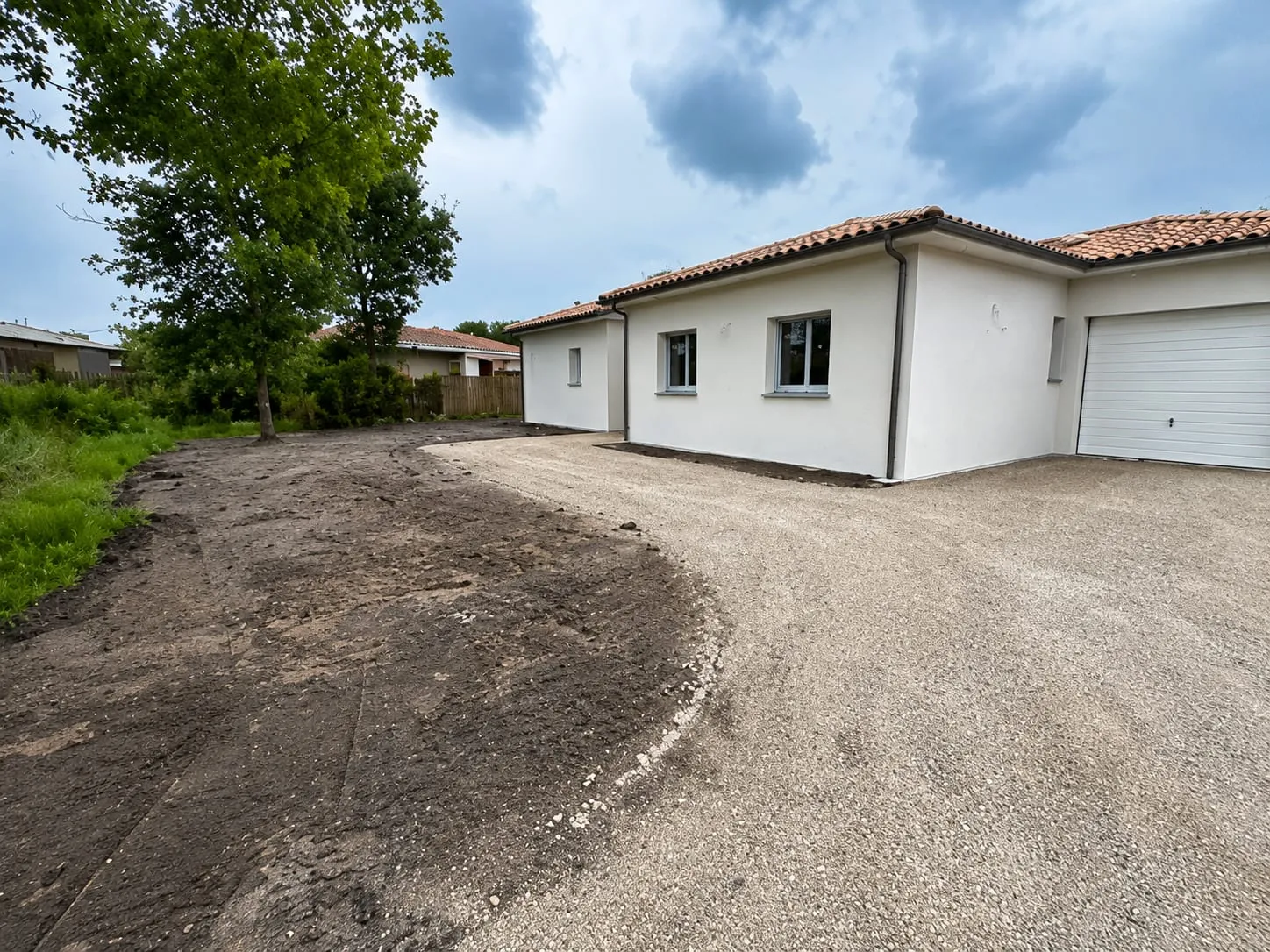 Accès en grave et terrain réglé autour d’une maison blanche