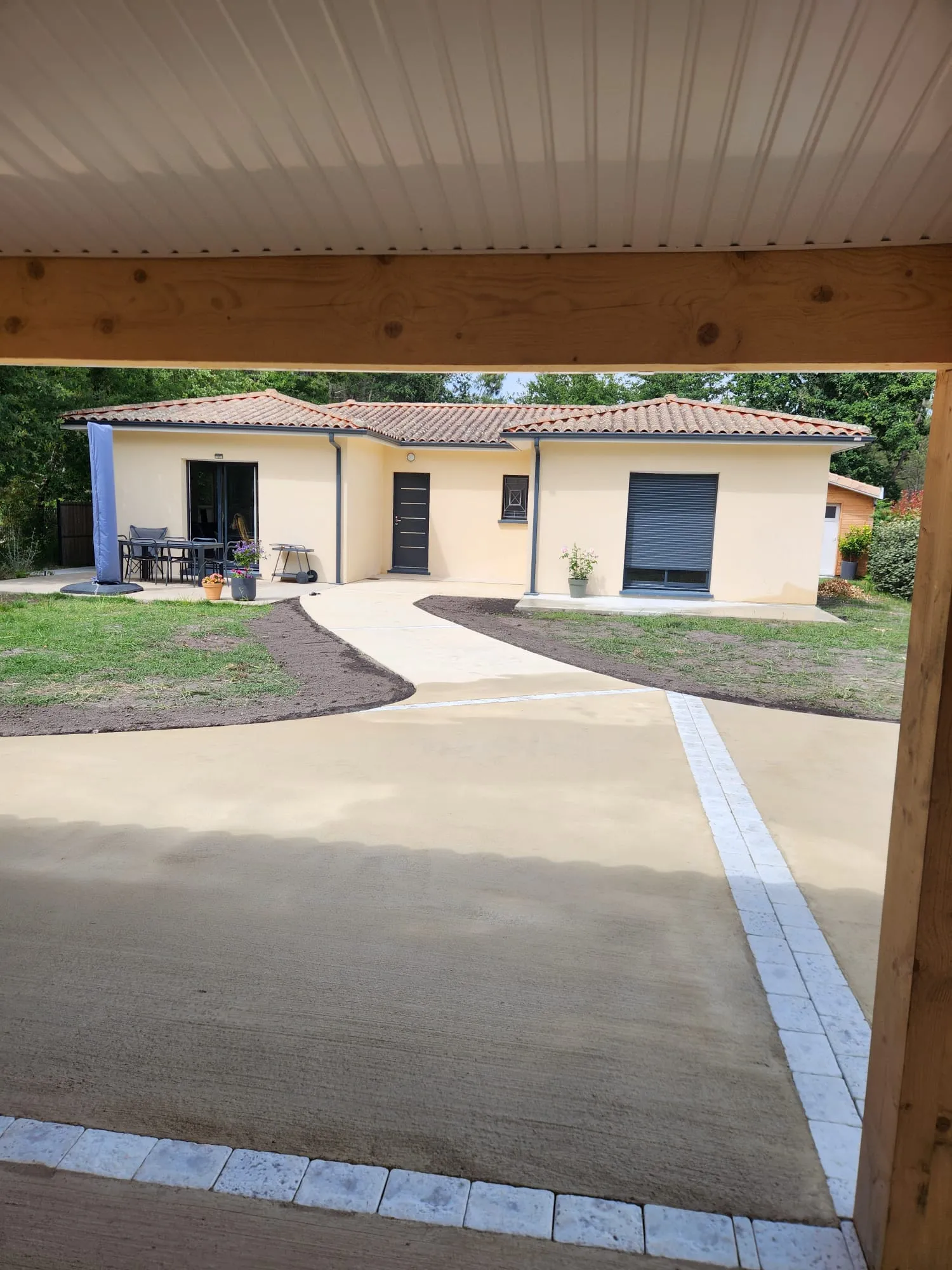 Allée en béton balayé sinueuse devant une maison médocaine avec carport en bois
