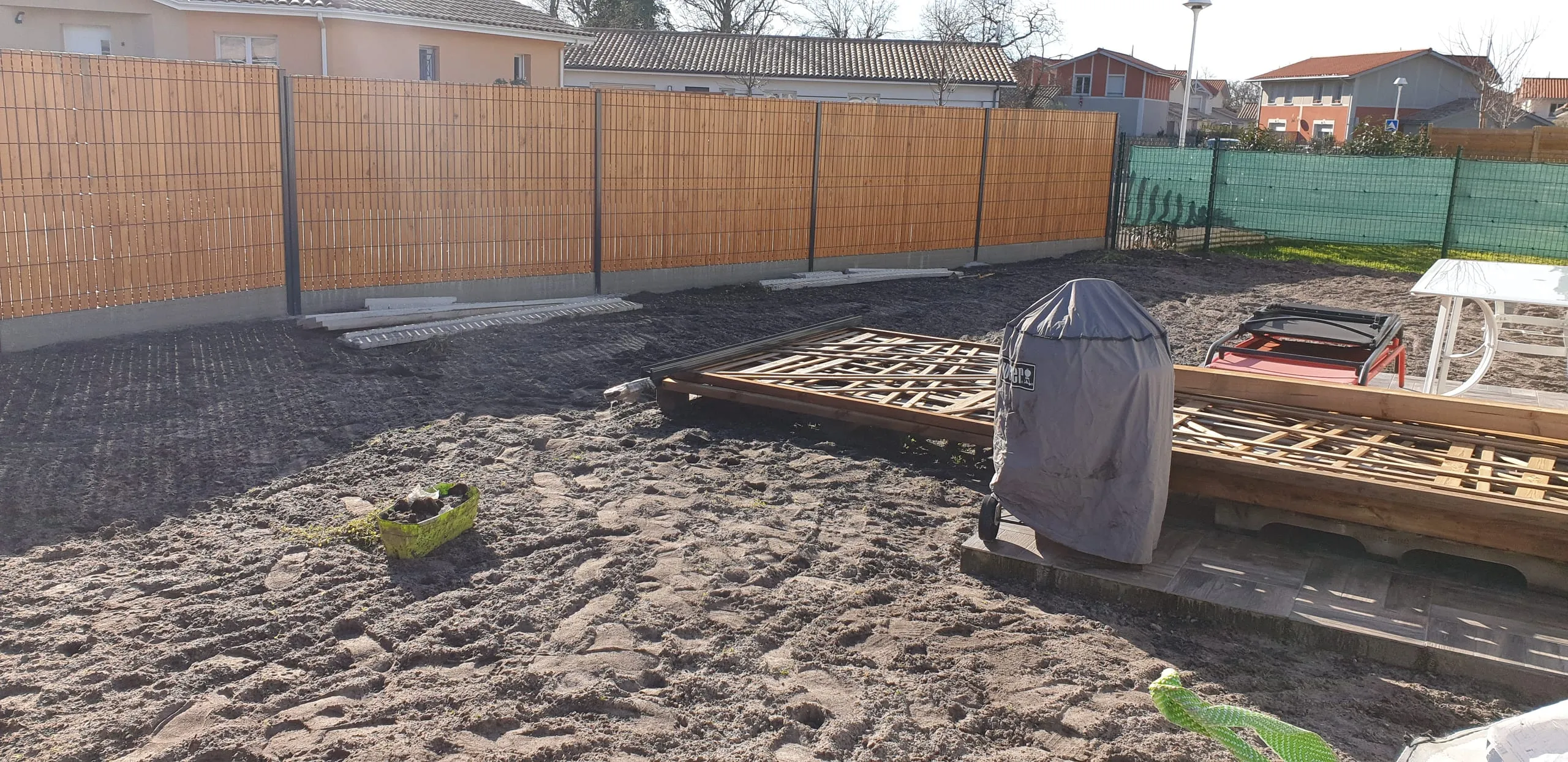Chantier de pose de clôture en palissade de bambou, poteaux en cours de scellement dans un jardin résidentiel