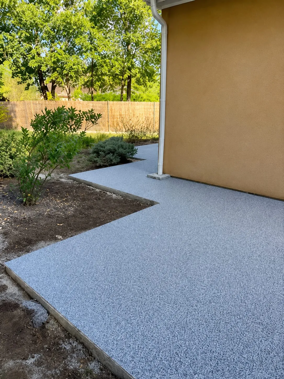 Chemin gris en résine longeant une maison et contournant les massifs du jardin