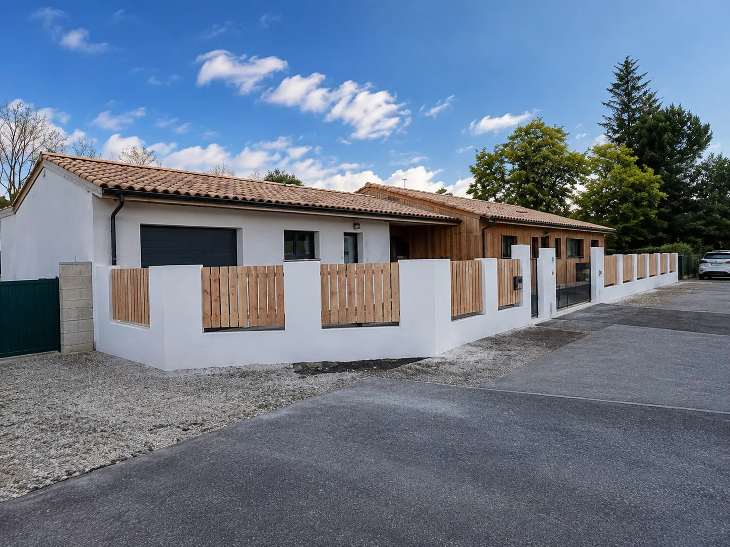 Clôture à lames de bois entre piliers blancs devant une maison