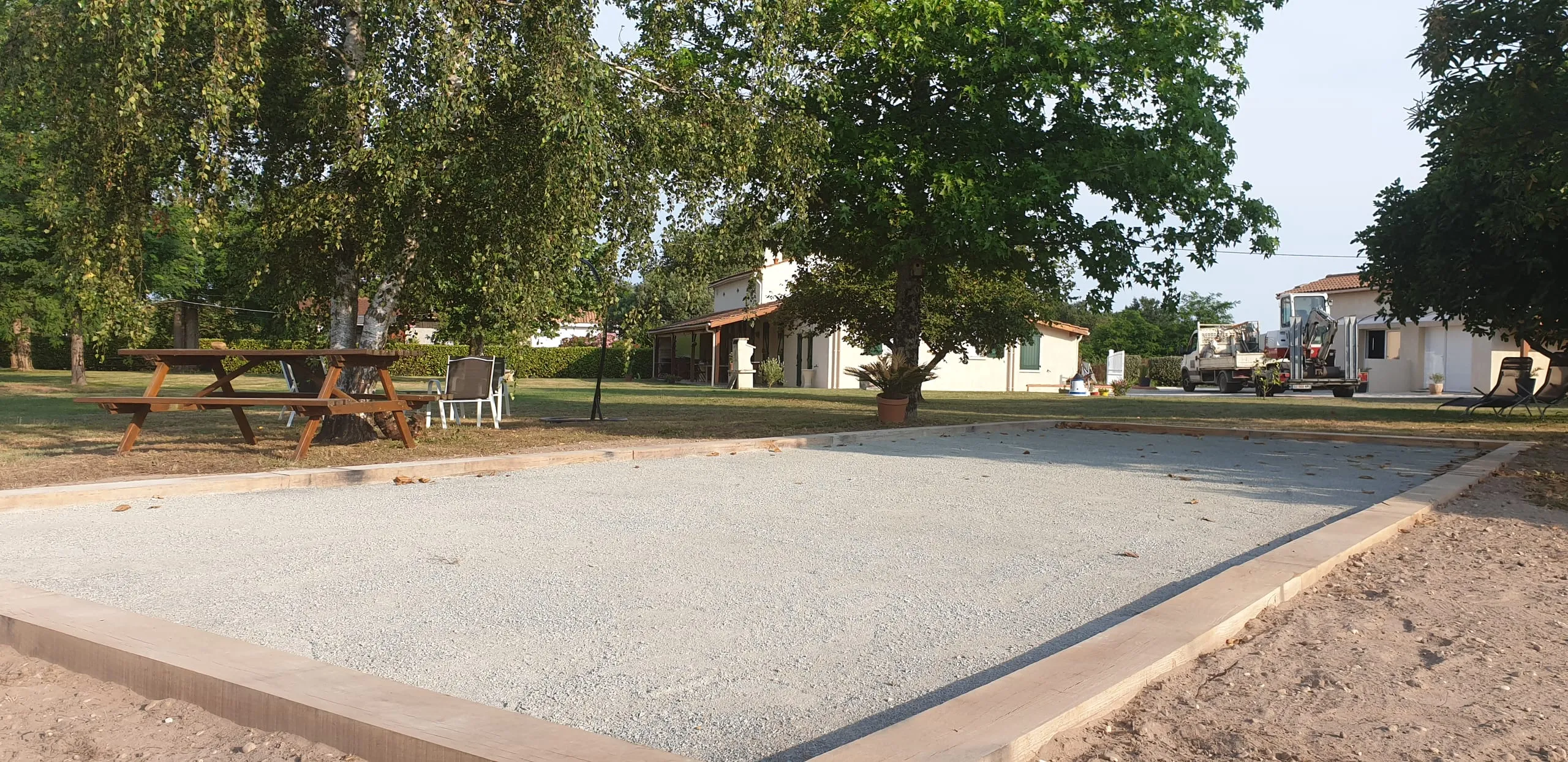 Grand terrain de pétanque en graviers avec bordures, arbres en fond