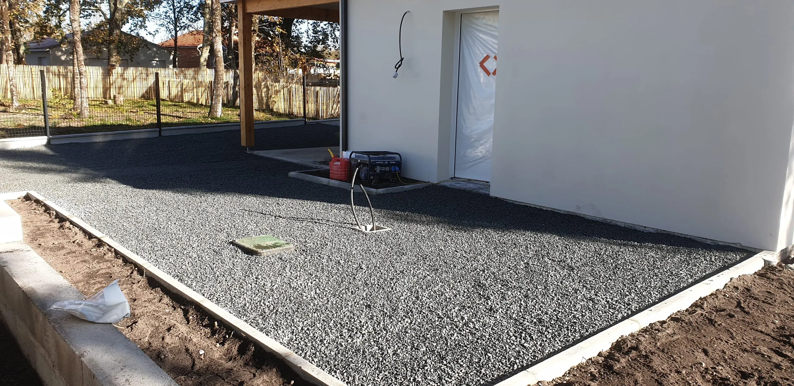 Parking en graviers gris avec bordures blanches, maison neuve à côté