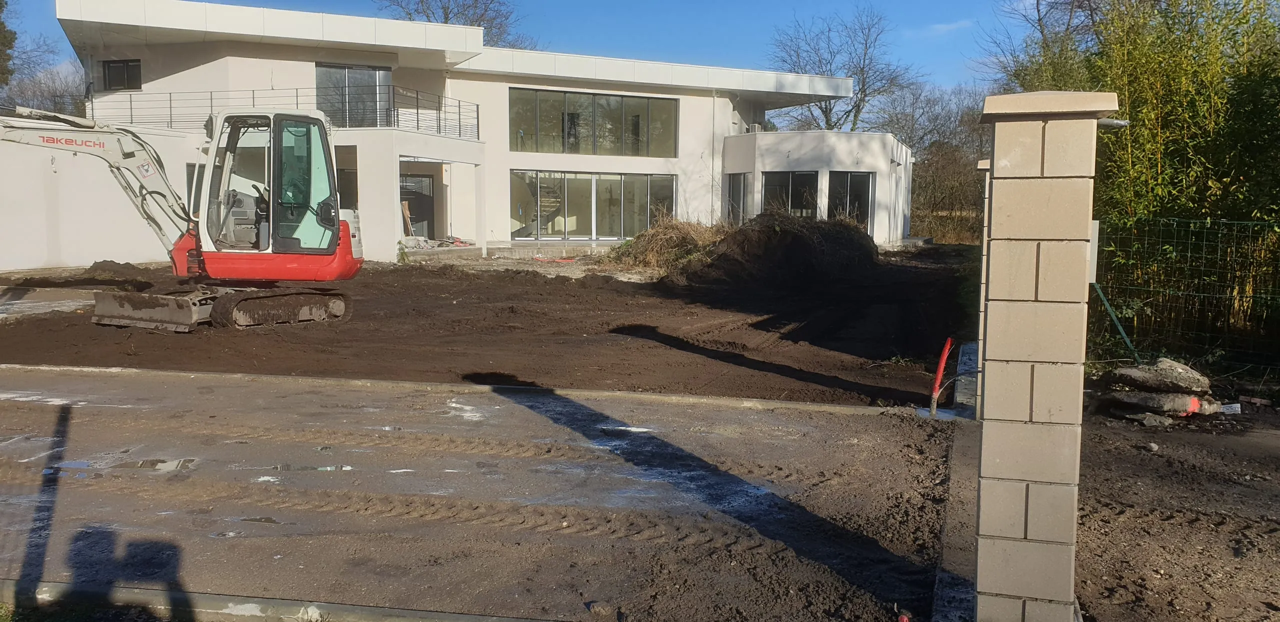 Mini-excavatrice Takeuchi sur chantier devant une grande villa contemporaine