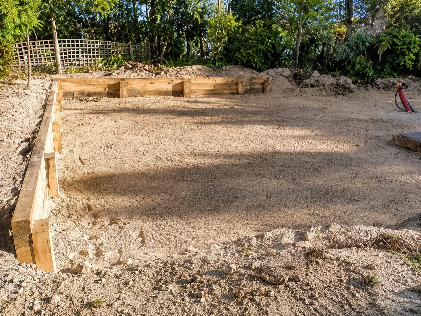 Plateforme de terre nivelée et maintenue par un coffrage en bois dans un jardin arboré