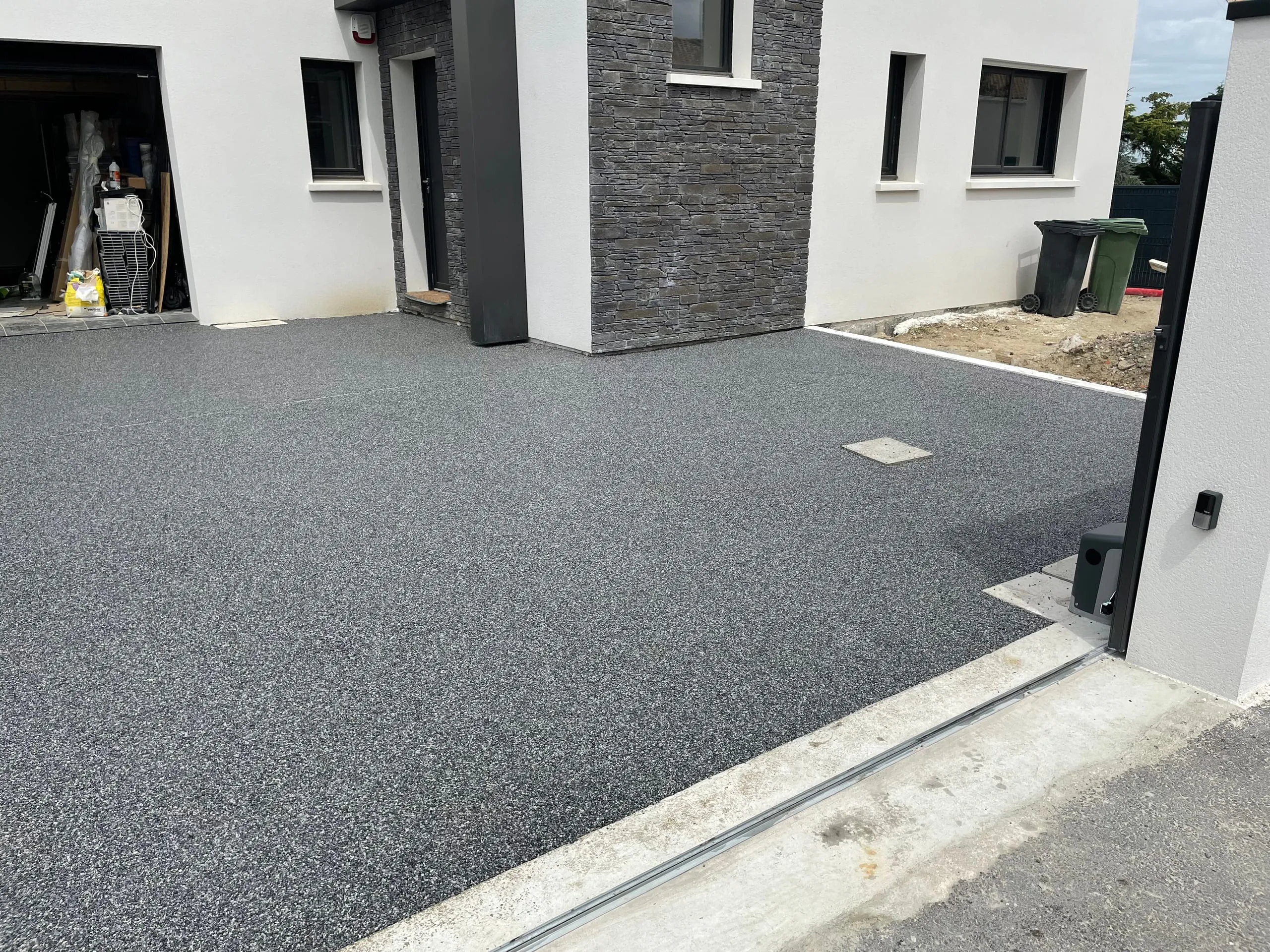 Grande cour en résine grise moquette de pierre devant maison moderne