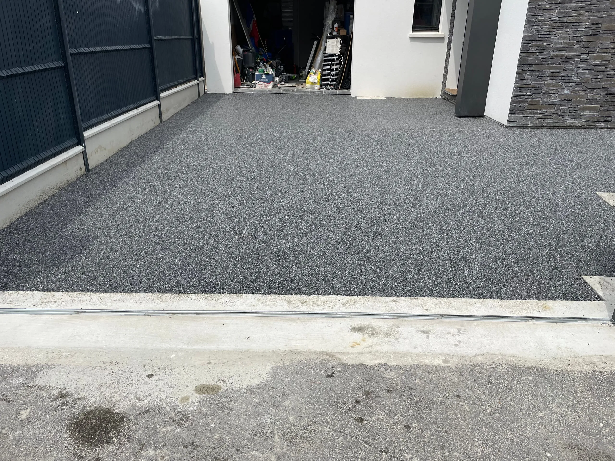 Cour de maison avec surface en résine gris anthracite, finition nette au seuil du garage et au guide de portail coulissant